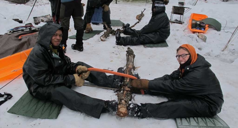 Two people work together to saw a log in a snowy landscape